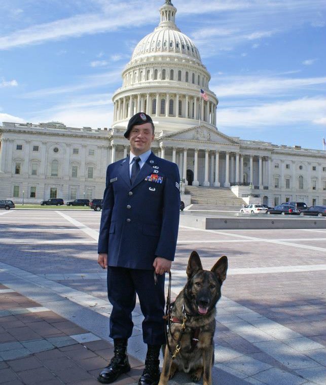 SrA Michael M. in uniform and sable guide dog "Xxon" mouth open tongue out standing in front of the US capitol building.