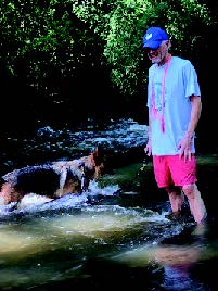 David stands in a stream with his guide dog Vixen