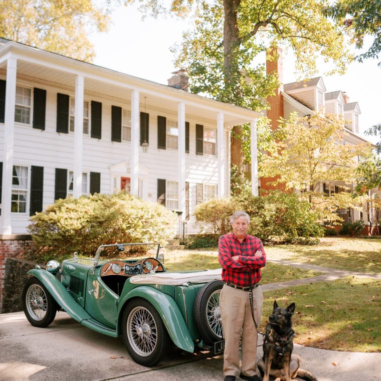 fidelco client steve smiling with his guide dog cricket sitting by his feet in front of his vintage car