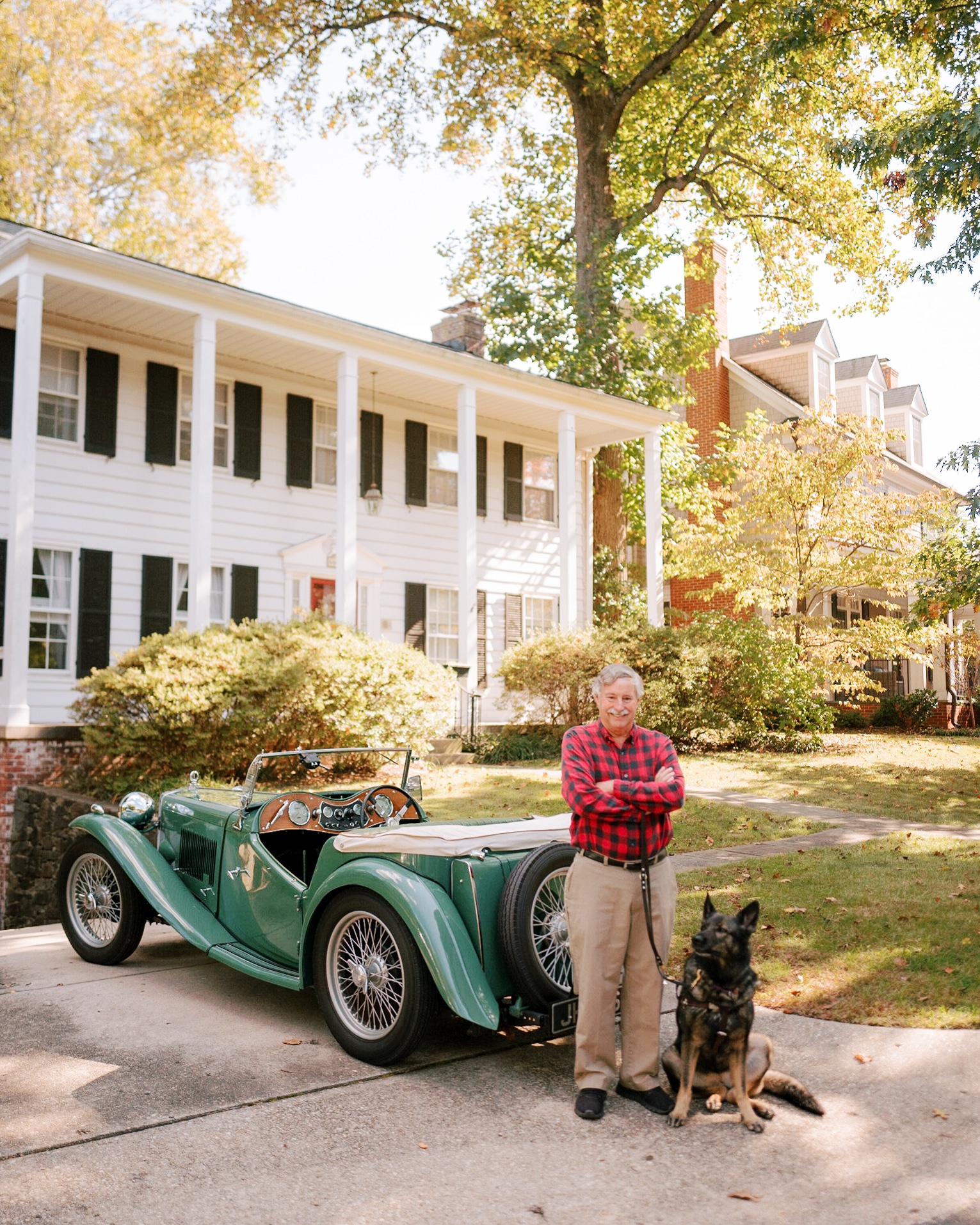 fidelco client steve smiling with his guide dog cricket sitting by his feet in front of his vintage car