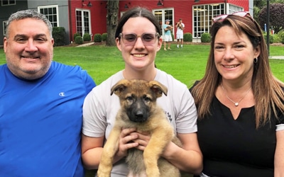 Three puppy raisers, two middle aged parents and their daughter holding a 3 month old puppy.