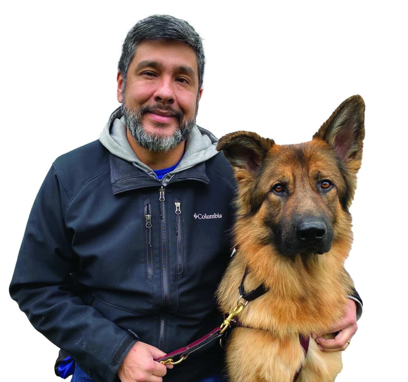 Miguel sitting and smiling while looking at camera with "Iron," a sable GSD, sitting to the right.