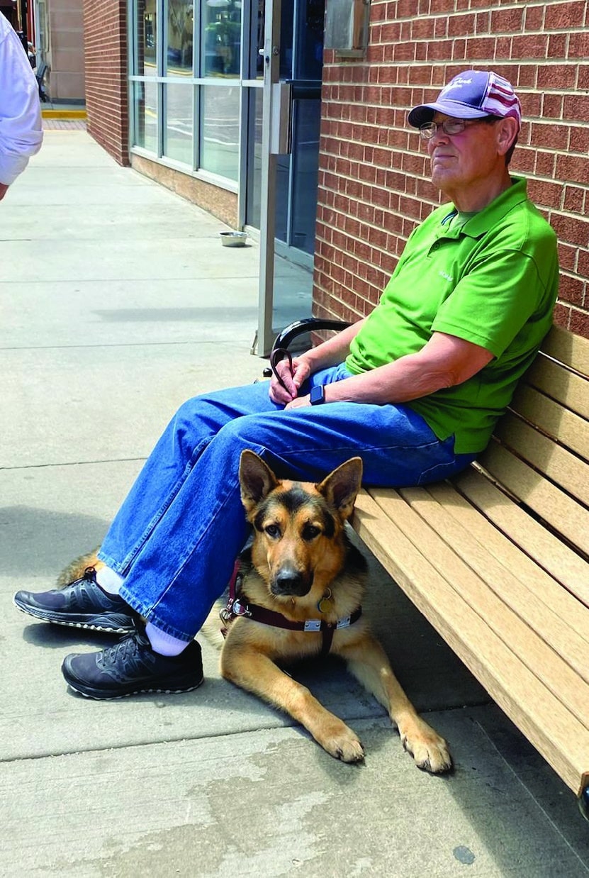 jim hoxie and dax under his legs while he sits on a bench