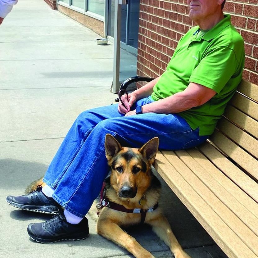 jim hoxie and dax under his legs while he sits on a bench