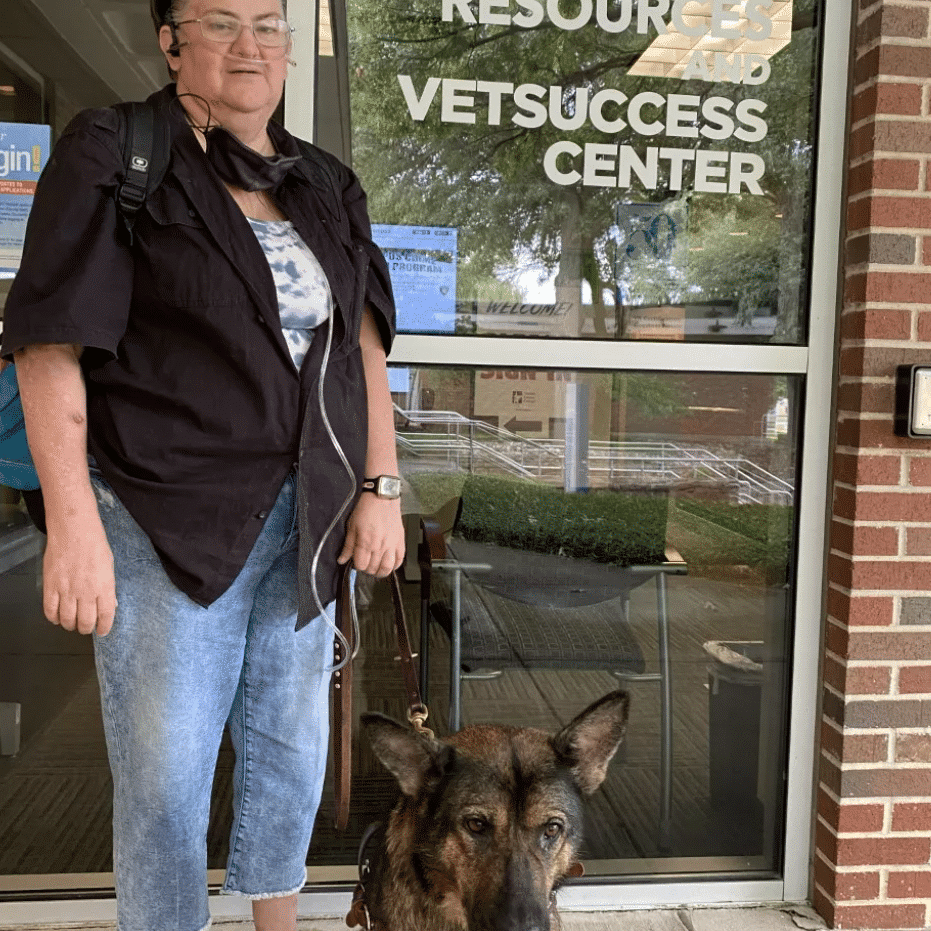 Jamie stands holding Haddie's leash as she sits in front of the student accessibility resources and vetsuccess center. 